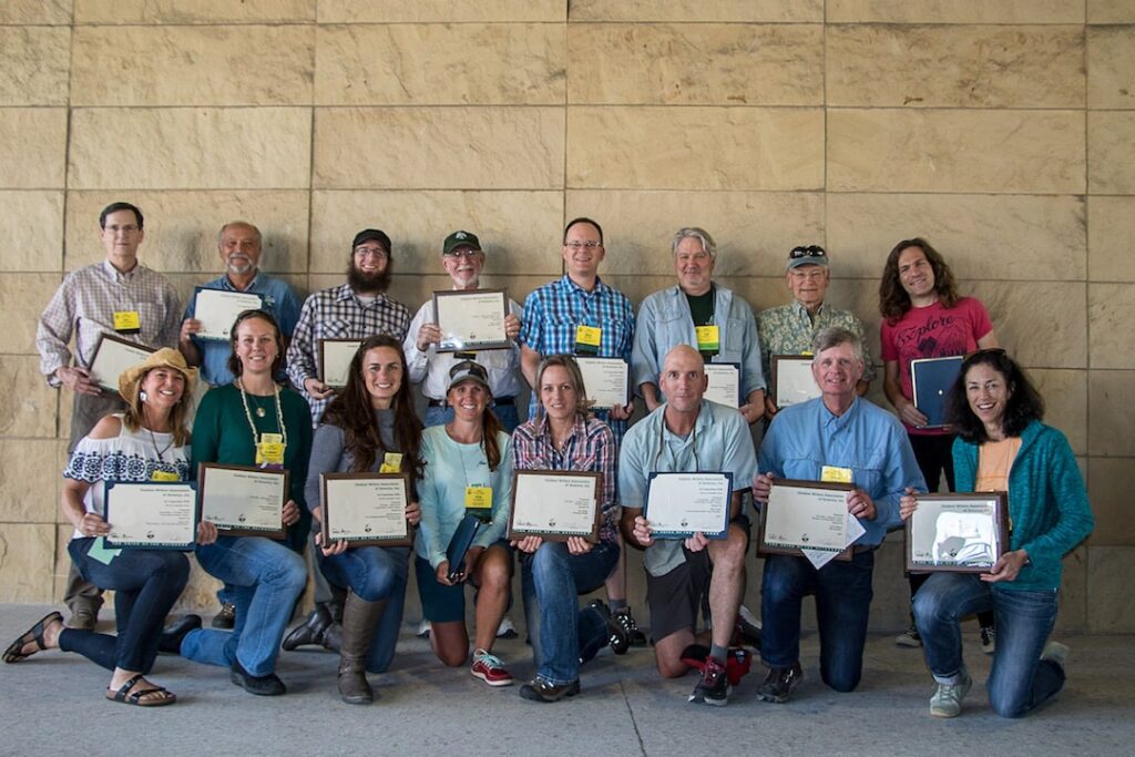 Two rows of winners of the OWAA Excellence in Craft award pose with plaques